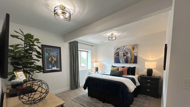 A bedroom with a bed, bedside tables, a plant, a framed picture, and a ceiling light fixture. - USAFA Retreat, 4BR/ 4BA, Front Range Views, Nestled in the Pines (Monument)