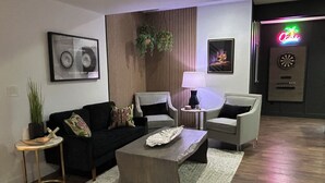 A modern living room with a black sofa, two armchairs, a coffee table, and a lamp. There is a framed picture on the wall, a plant, and a neon sign in the background. - USAFA Retreat, 4BR/ 4BA, Front Range Views, Nestled in the Pines (Monument)
