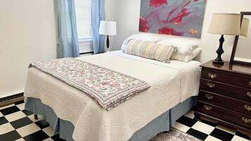 Une chambre à coucher avec un lit, une table de chevet, une lampe, un tableau et un tapis à motifs.
