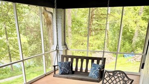 A covered outdoor seating area with a table and two chairs, a swing, and a view of a wooded area. - Farmville Lake House minutes from H-SC and Longwood (Farmville)