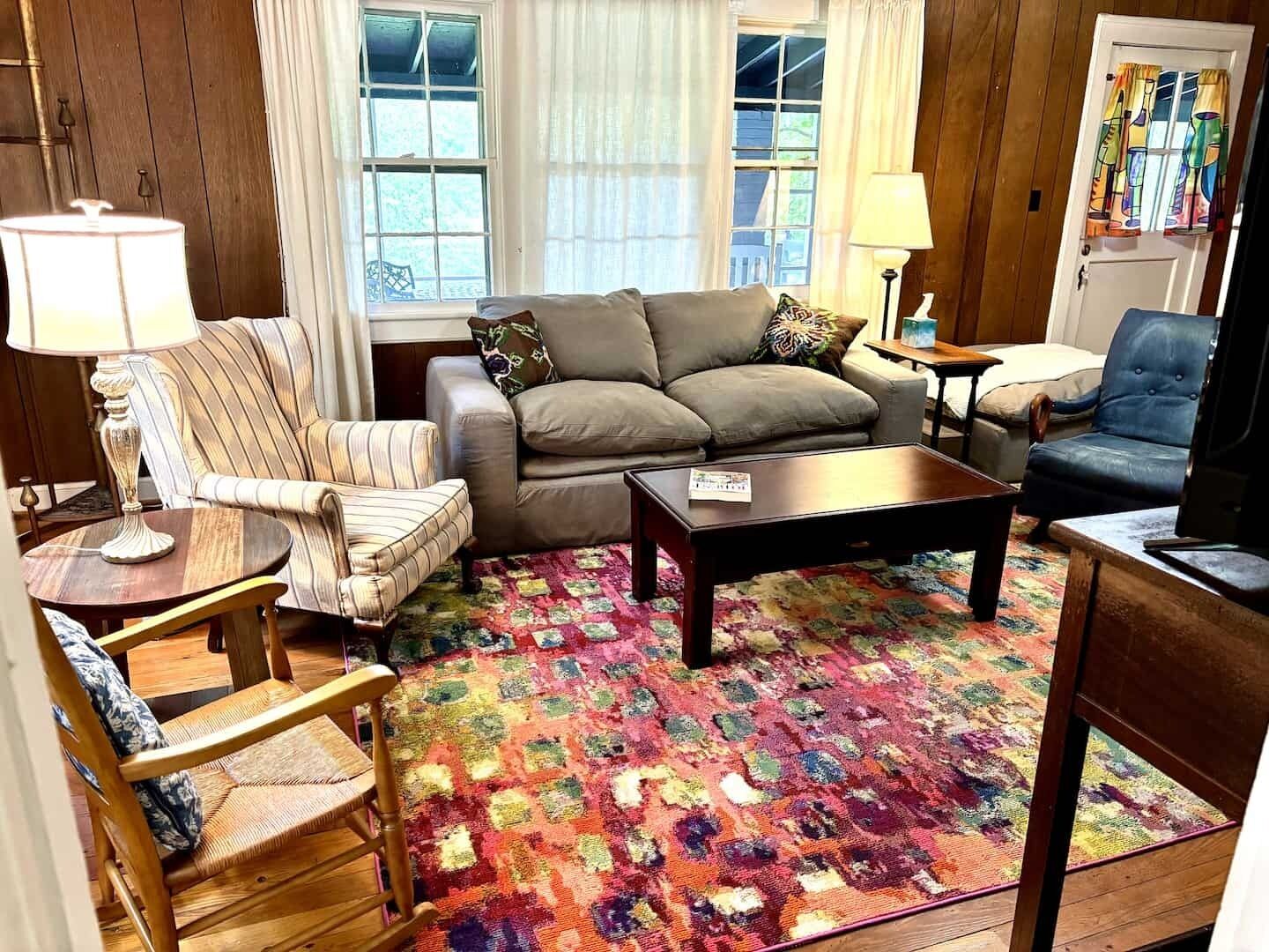Un salon comprenant un canapé, des fauteuils, une table basse et un tapis à motifs.