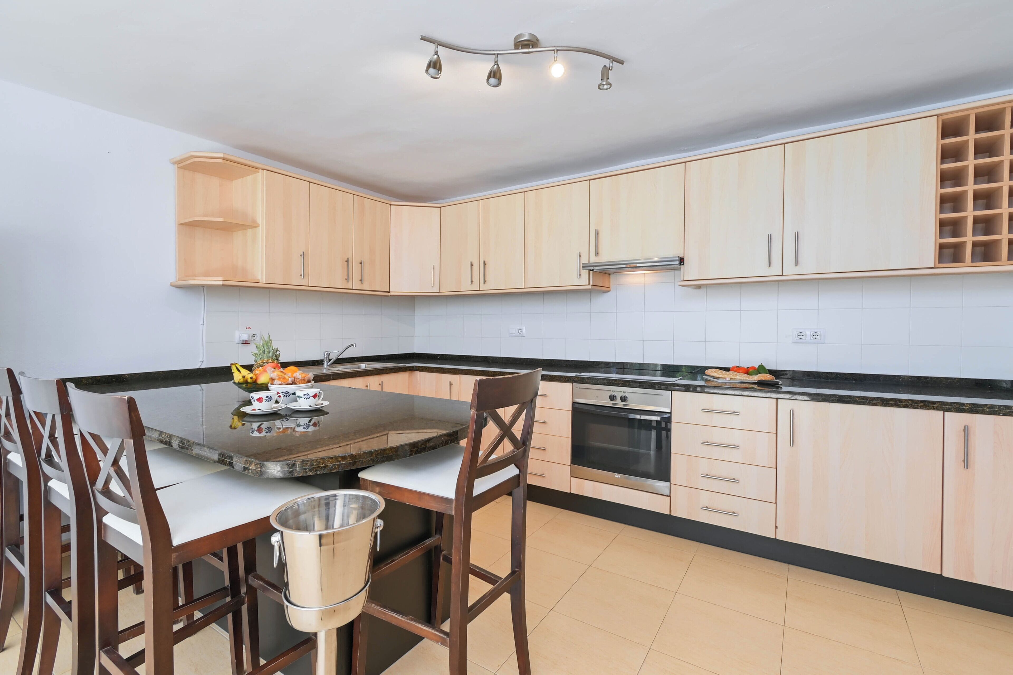 A modern kitchen with light wood cabinets, a stainless steel oven, and a dining area with a table and chairs.