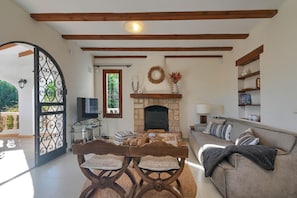 A living room with a fireplace, a sofa, a TV, and a dining table with chairs. - Casa Amandine, within walking distance of La Fustera Beach (Benissa)