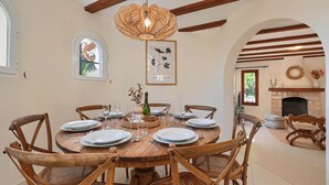 A dining area with a round wooden table set for six, surrounded by six wooden chairs with woven seats. - Casa Amandine, within walking distance of La Fustera Beach (Benissa)