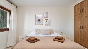 A bedroom with a bed, two pillows, a nightstand, a wooden wardrobe, and two framed artworks on the wall. - Casa Amandine, within walking distance of La Fustera Beach (Benissa)