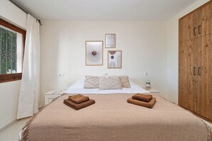 Ein Schlafzimmer mit einem Bett, zwei Kissen, einem Nachttisch, einem Holzschrank und zwei gerahmten Kunstwerken an der Wand.