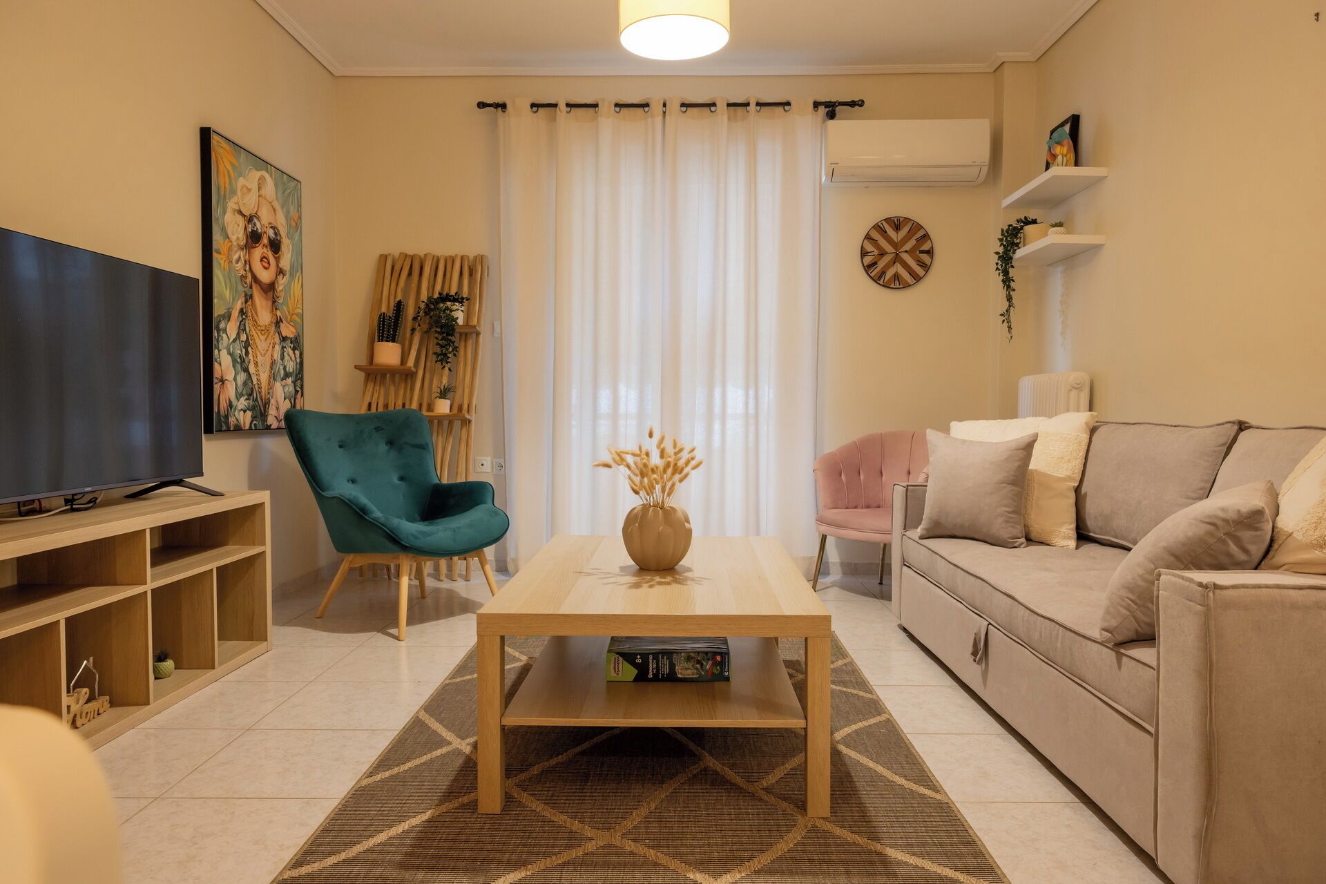 A living room with a television, a teal armchair, a wooden coffee table, a beige sofa, and a patterned rug.
