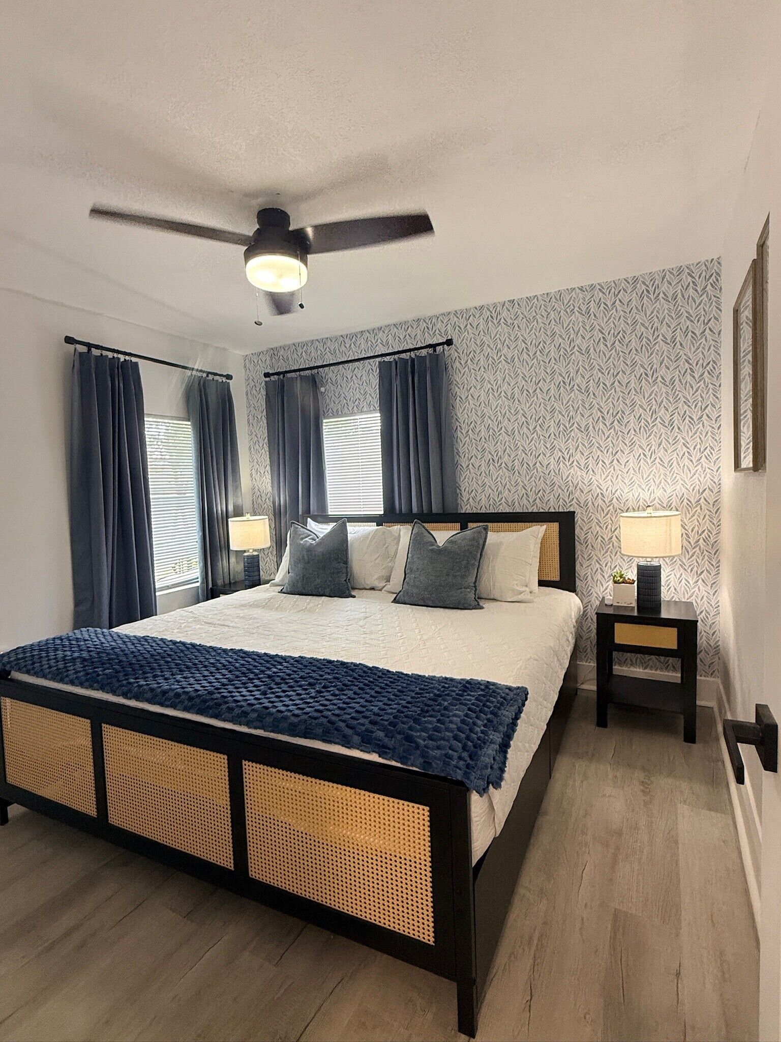 A bedroom with a bed, two bedside tables, a ceiling fan, and patterned wallpaper.
