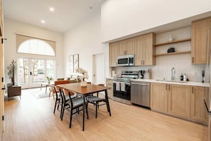 A modern kitchen with wooden cabinets, stainless steel appliances, and a dining area with a wooden table and chairs.