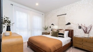 A modern bedroom with a large bed, wooden nightstands, a bedside table, and a wall-mounted lamp.