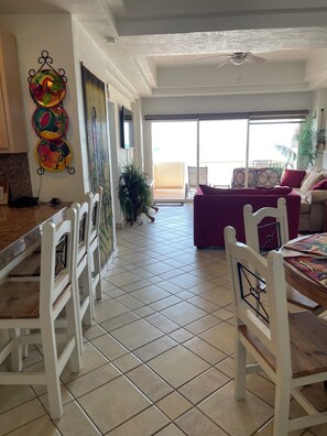 A dining area with white chairs, a table, and a colorful wall decoration. - 1-bedroom Sandy Beach condo with ocean view and AC (Puerto Peñasco)