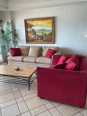 Ein Wohnzimmer mit einer Couch, einem roten Sessel, einem Couchtisch und einem Bild an der Wand.