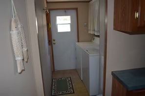 A laundry room with a washing machine, a door with a window, and a patterned rug on the floor. - Sunset Bay Waterfront Retreat (Springville)