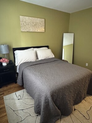 A bedroom with a bed, a nightstand, a lamp, and a mirror.