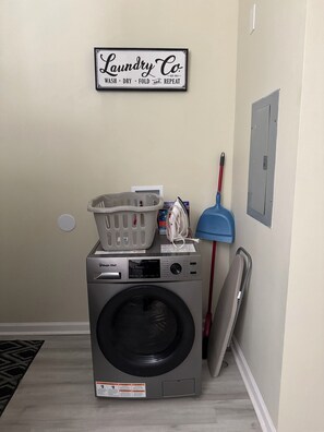 A laundry area with a washing machine, a laundry basket, a mop, and a sign above the machine.