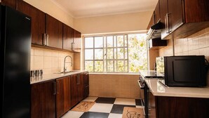 Une cuisine avec des meubles en bois foncé, un réfrigérateur noir, un four à micro-ondes et une fenêtre donnant sur un paysage verdoyant.