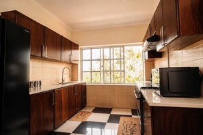 Une cuisine avec des meubles en bois foncé, un réfrigérateur noir, un four à micro-ondes et une fenêtre donnant sur un paysage verdoyant.