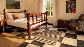 Une chambre à coucher avec un lit en bois, un fauteuil à motifs, un tapis et des œuvres d’art accrochées aux murs.