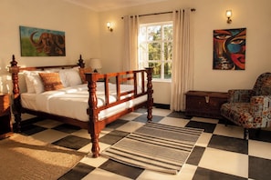 Une chambre à coucher avec un lit en bois, un fauteuil à motifs, un tapis et des œuvres d’art accrochées aux murs.