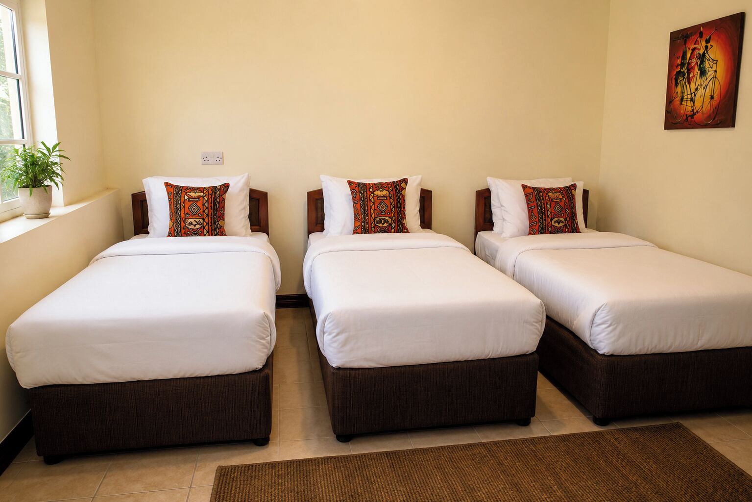 A hotel room with three single beds, a potted plant by the window, and a painting on the wall.