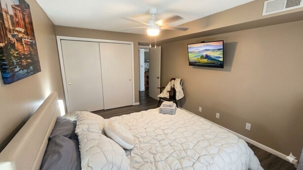 A bedroom with a bed, a ceiling fan, a TV on the wall, and a door leading to another room. - Wobbly Glaize Getaway! Cozy Lake Condo near Wobbly Boots and Grand Glaize Bridge (Osage Beach)