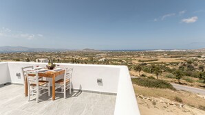 A terrace with a table set for two, overlooking a landscape with buildings and mountains.