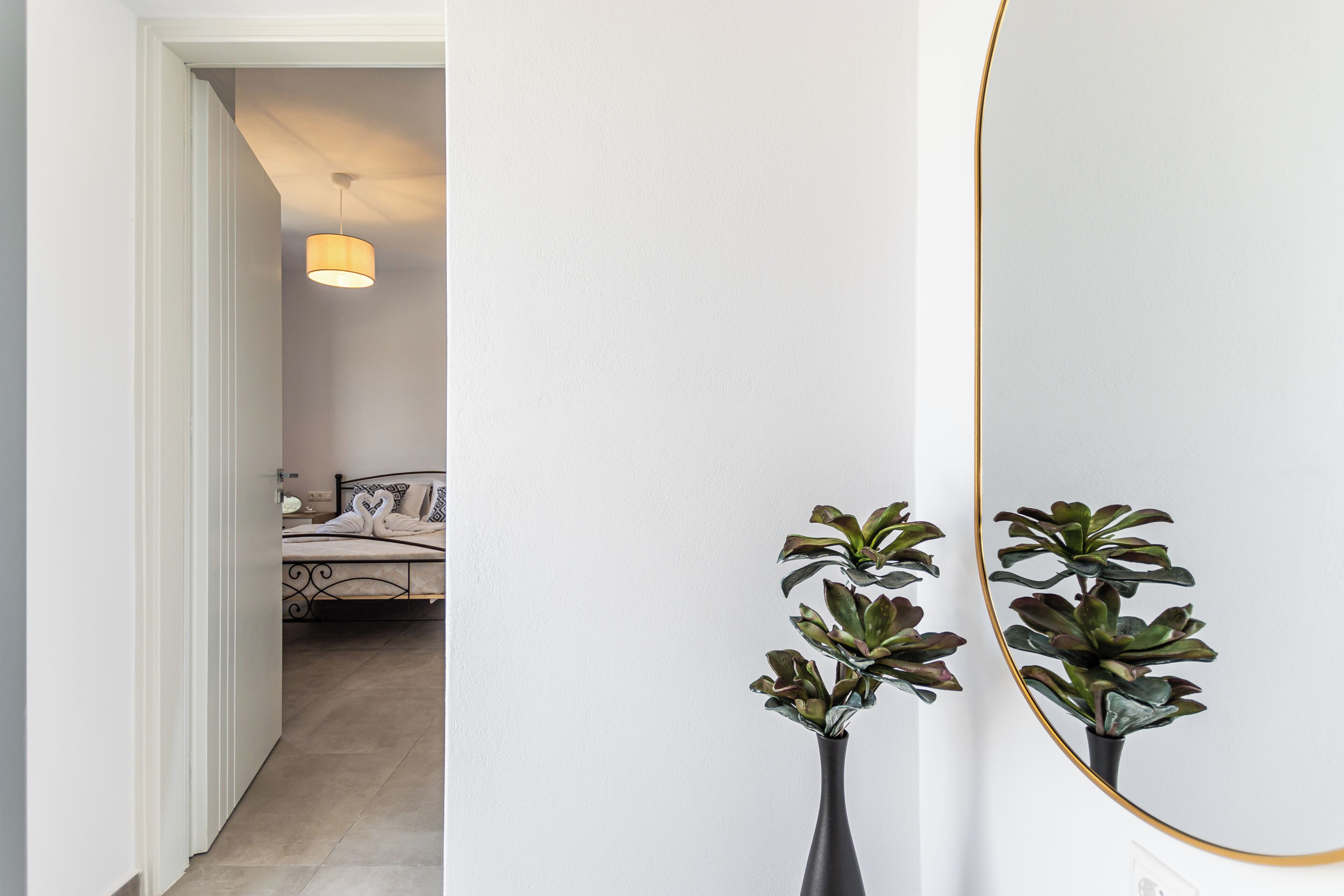 Un couloir avec un lit en arrière-plan, un miroir et deux plantes en pot.