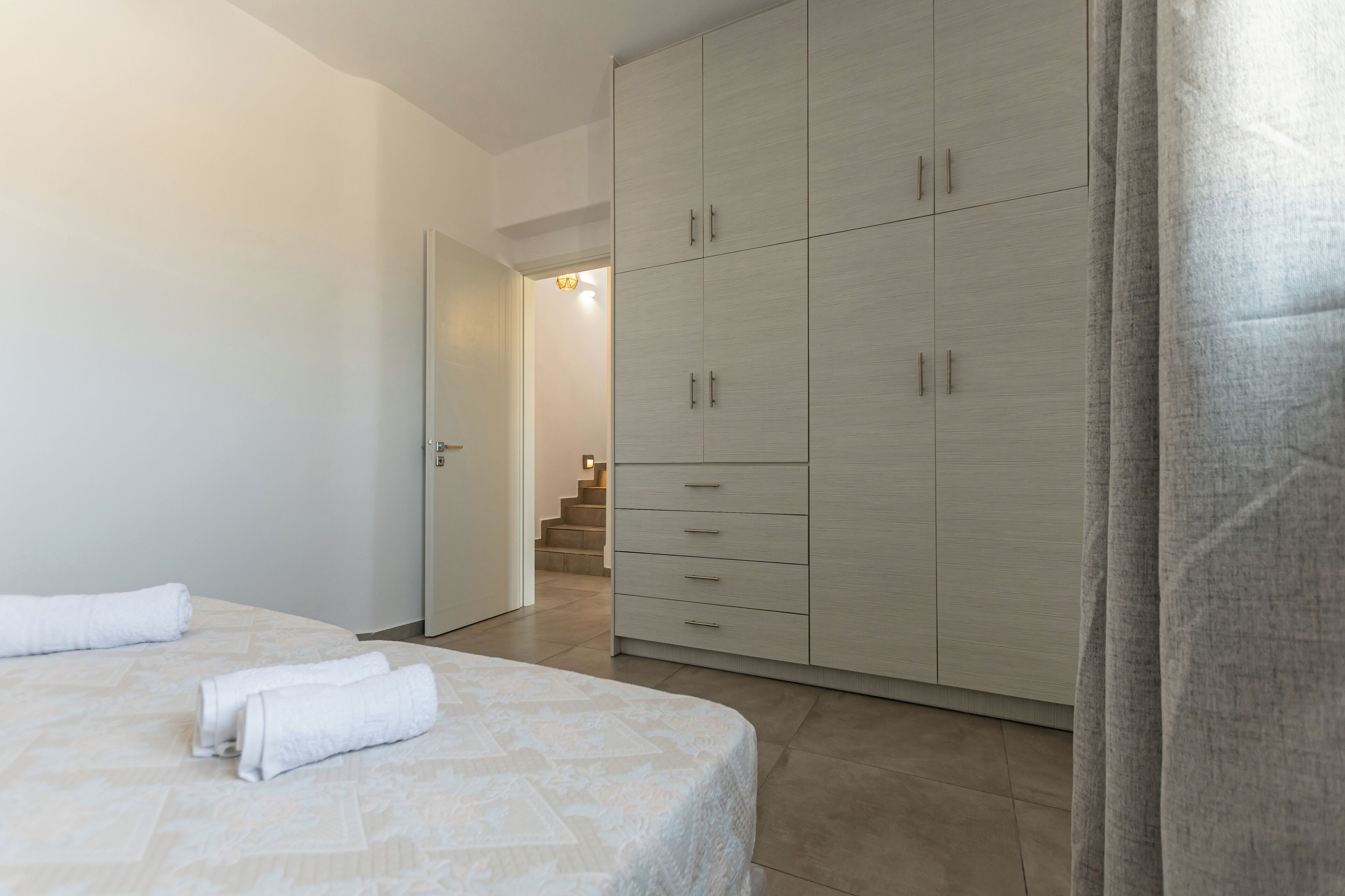 Une chambre dotée d’une grande armoire, d’un lit recouvert d’une couvre-lit à motifs et d’un escalier menant à l’étage supérieur.