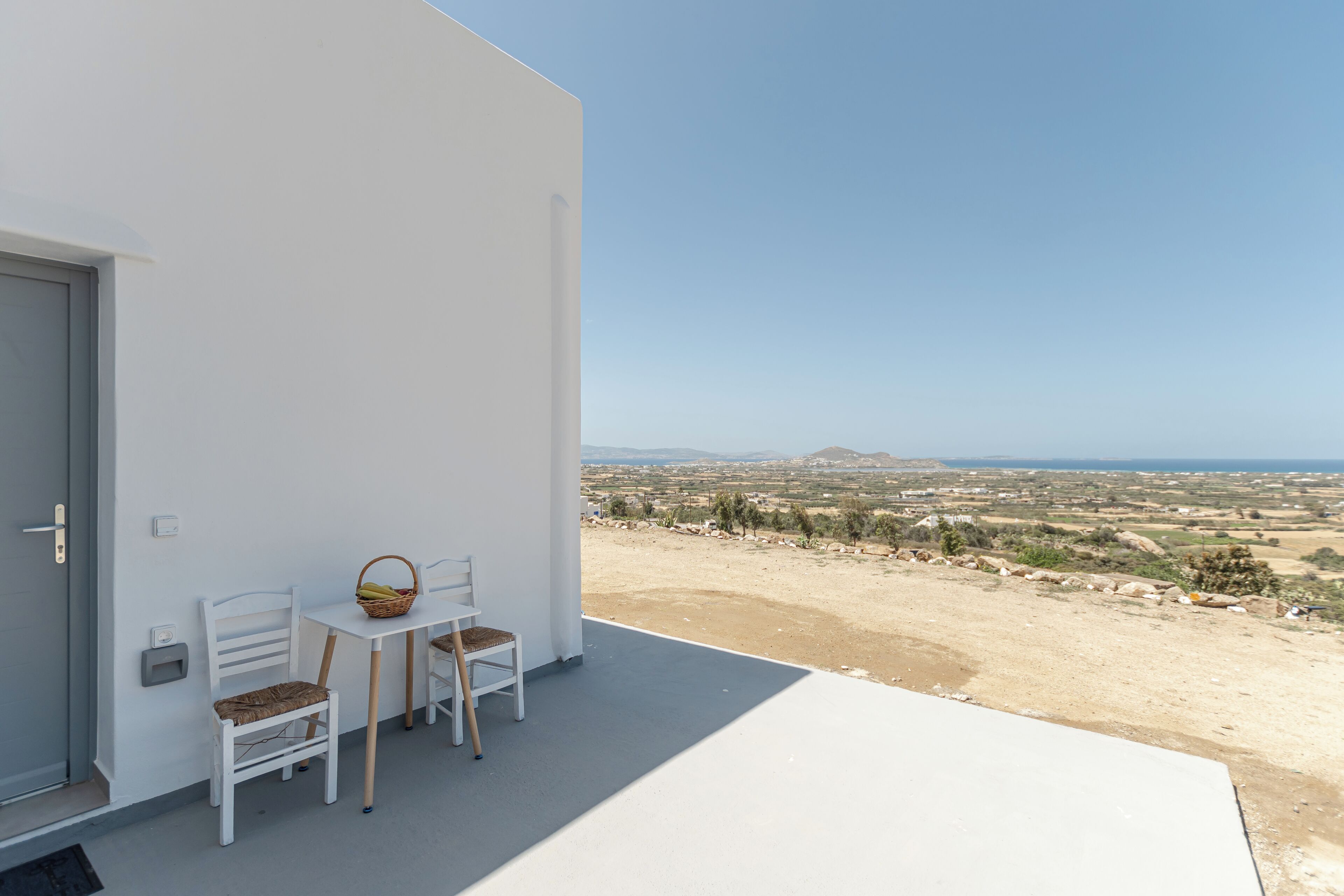 A balcony with two white chairs and a small table, overlooking a coastal landscape.