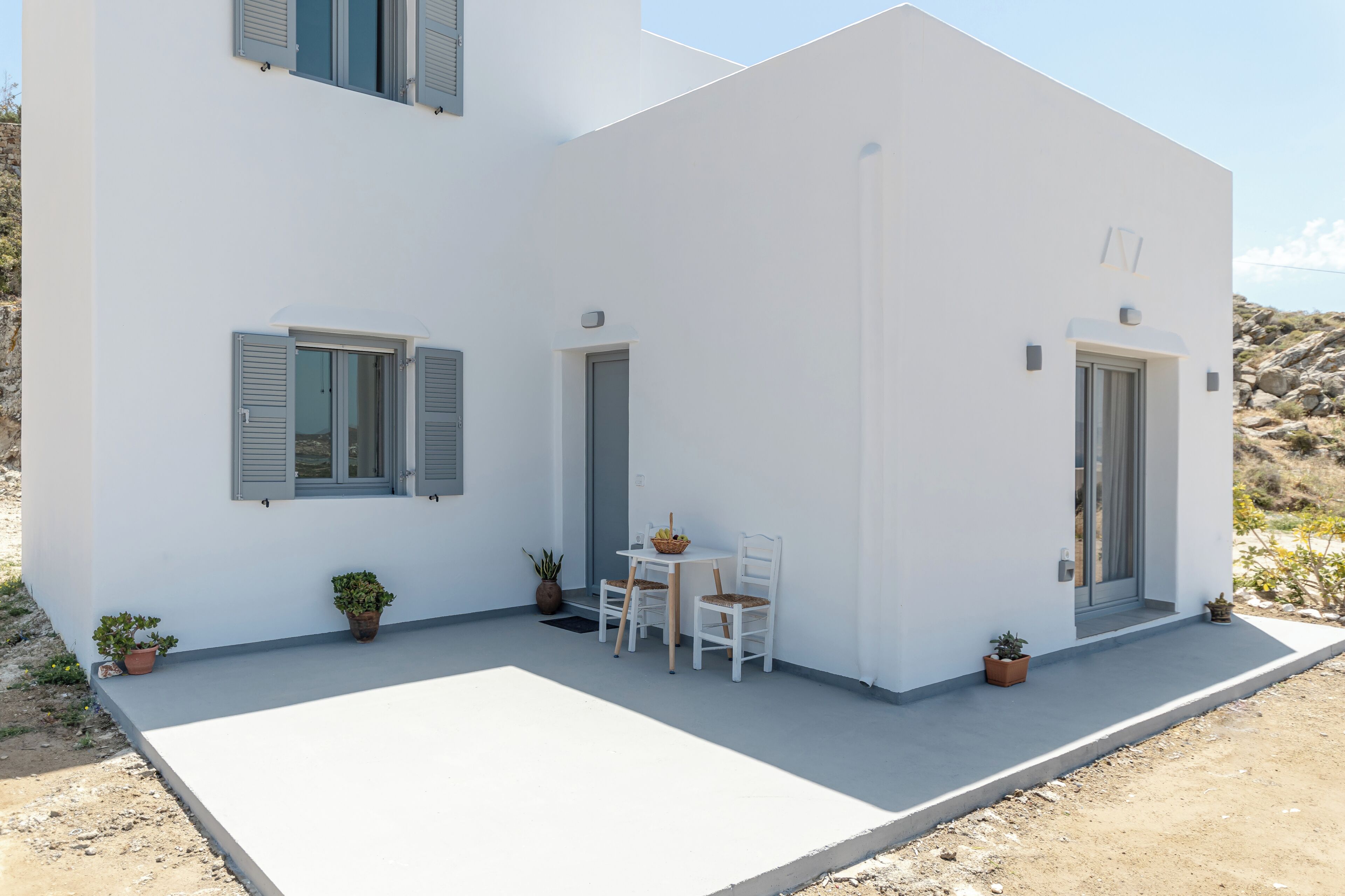 A modern two-story building with a flat roof, a balcony, and a small outdoor seating area with a table and chairs.