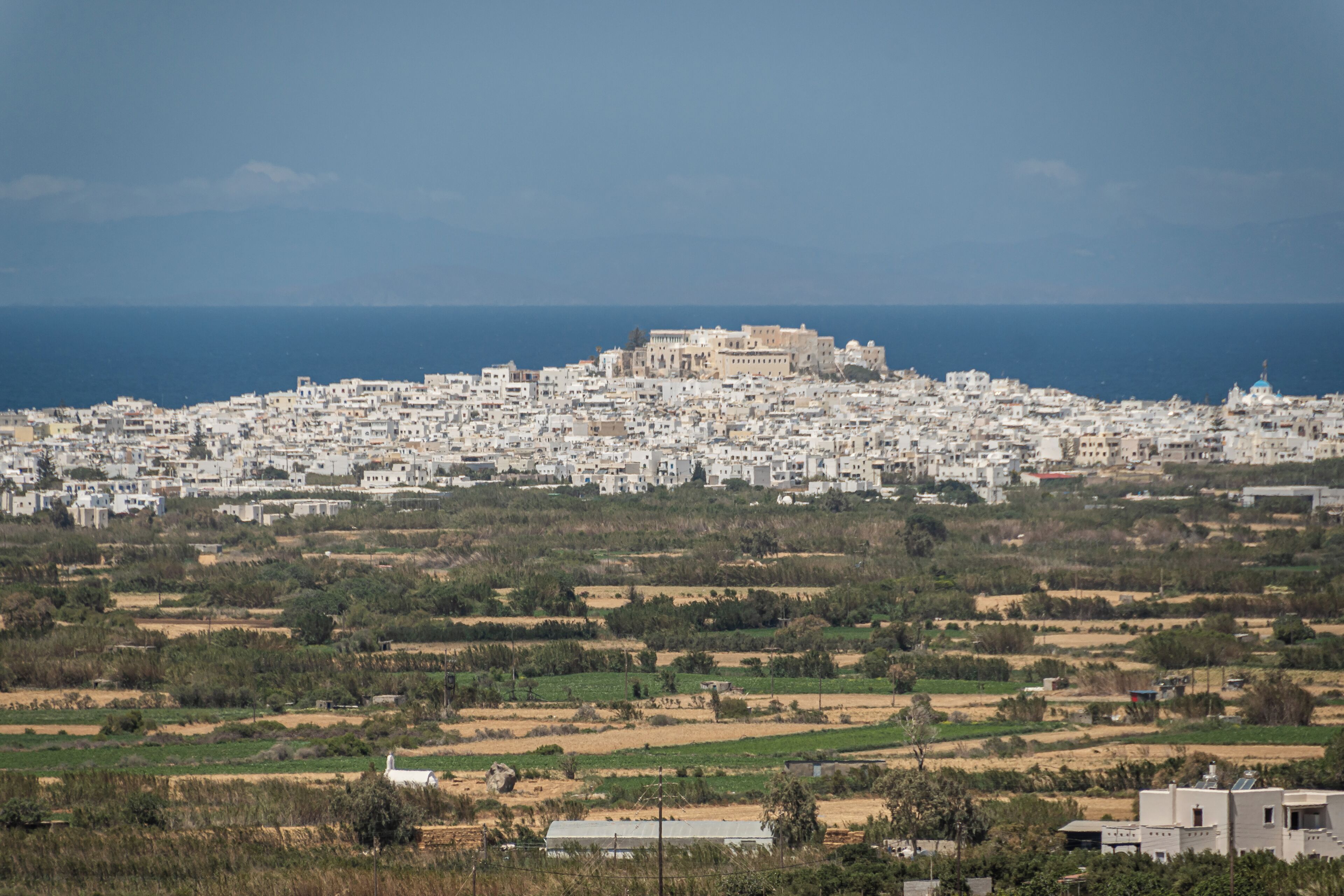 Un paysage urbain côtier, avec un bâtiment historique imposant situé sur une colline, entouré de zones résidentielles et de champs agricoles.