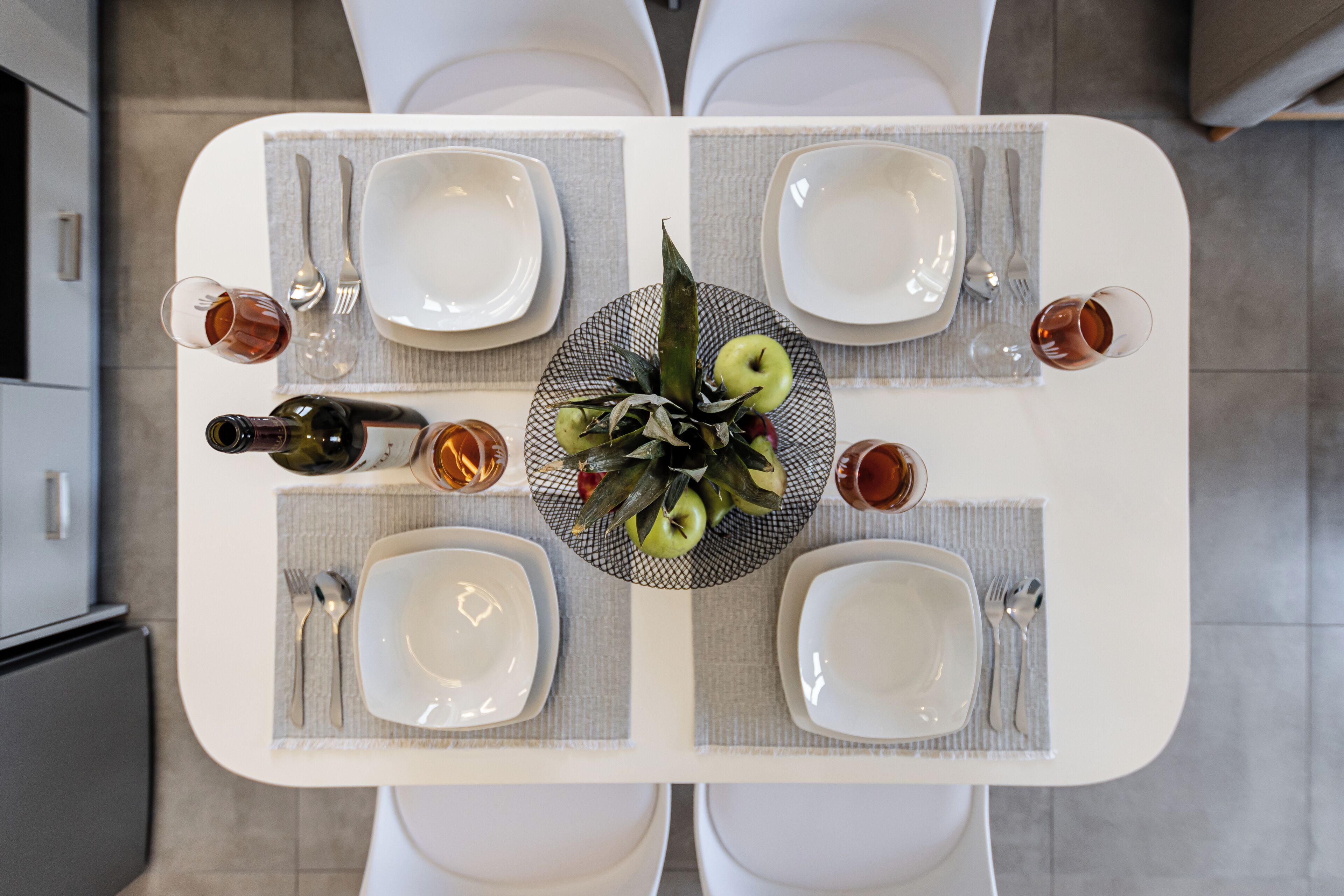Une table à manger dressée pour quatre personnes, avec de l’argenterie, des assiettes blanches et des verres, ainsi qu’une bouteille de vin.