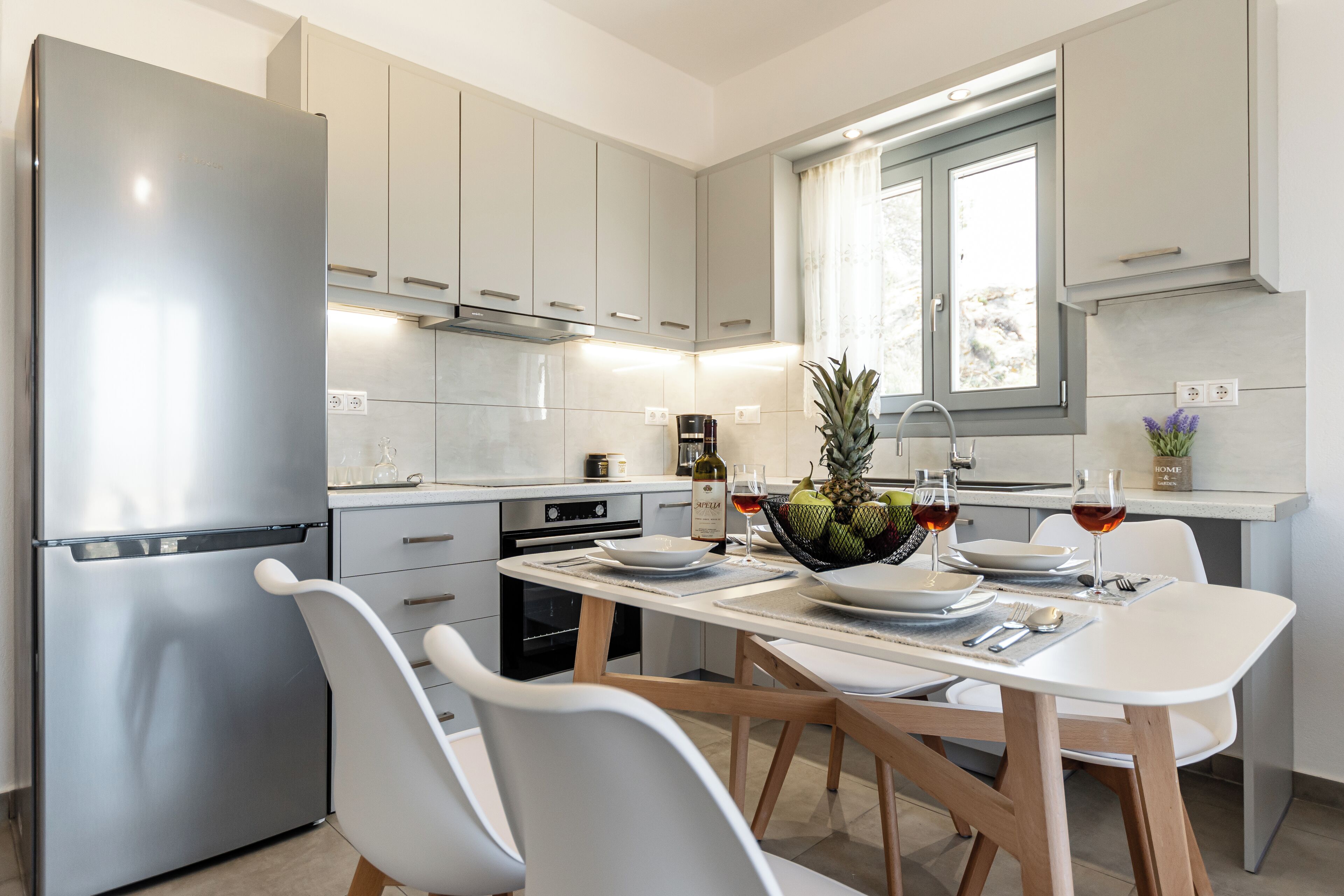 A modern kitchen with stainless steel appliances, white cabinetry, and a dining area set for two.