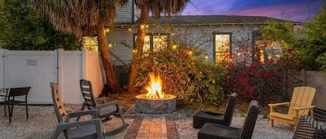 A patio area with outdoor seating, a fire pit, and a house in the background.