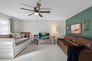 A living room with a ceiling fan, a television, a sofa, a coffee table, and a lamp. - Magnolia House; Grille/Firepit/Patio View! (Tampa)