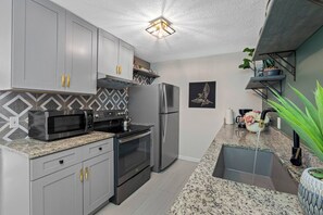A modern kitchen with grey cabinets, a stainless steel refrigerator, a microwave, and an oven. - Magnolia House; Grille/Firepit/Patio View! (Tampa)