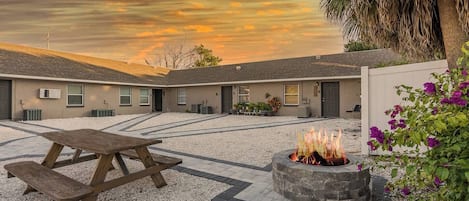 A courtyard with a fire pit, picnic table, and a building with multiple windows and a door.