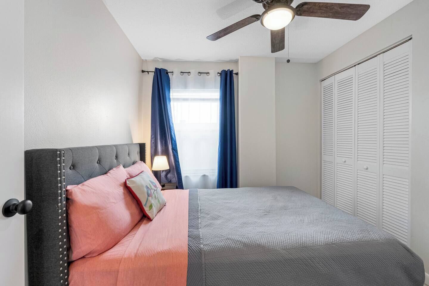 Ein Schlafzimmer mit einem Bett, Deckenventilator, einem Fenster mit Vorhängen und einem Kleiderschrank.