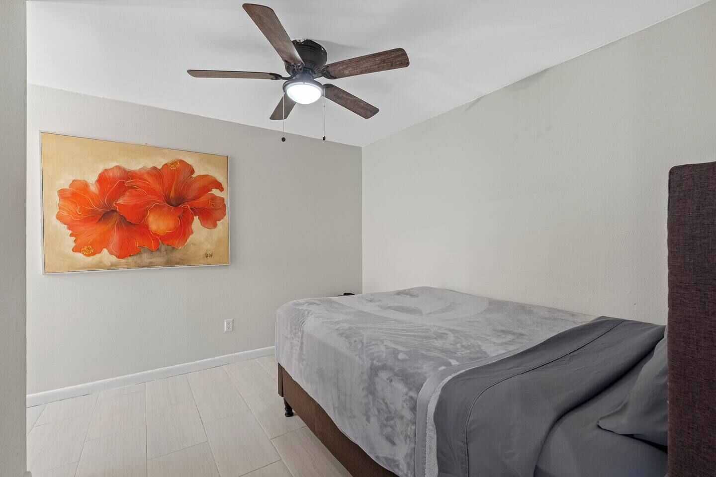 Een slaapkamer met een bed, een plafondventilator en een schilderij aan de muur.
