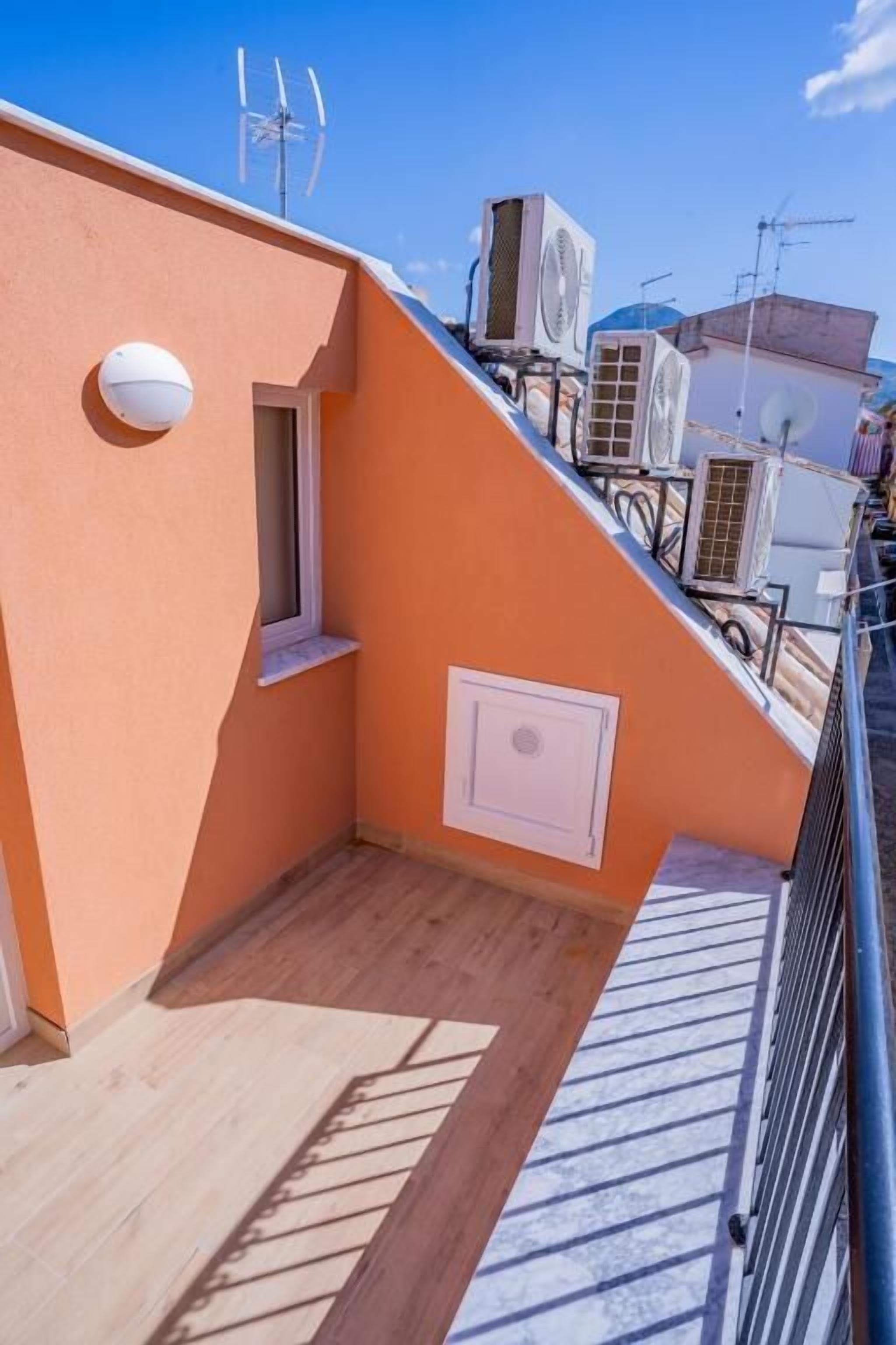 A rooftop terrace with a wooden floor, a small window, and an air conditioning unit.