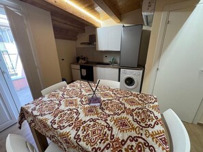 Un comedor con mantel estampado, lavadora y cocina equipada con armarios y refrigerador.