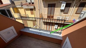 Un balcón con barandilla de metal, una ventana pequeña y una puerta blanca.
