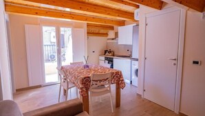Una habitación con mesa de comedor, sillas, sofá, zona de cocina con armarios y una puerta.