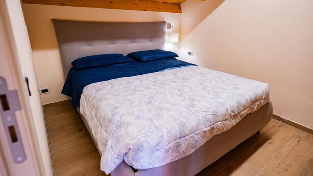 Un dormitorio con una cama, techo de madera y una lámpara fijada a la pared.