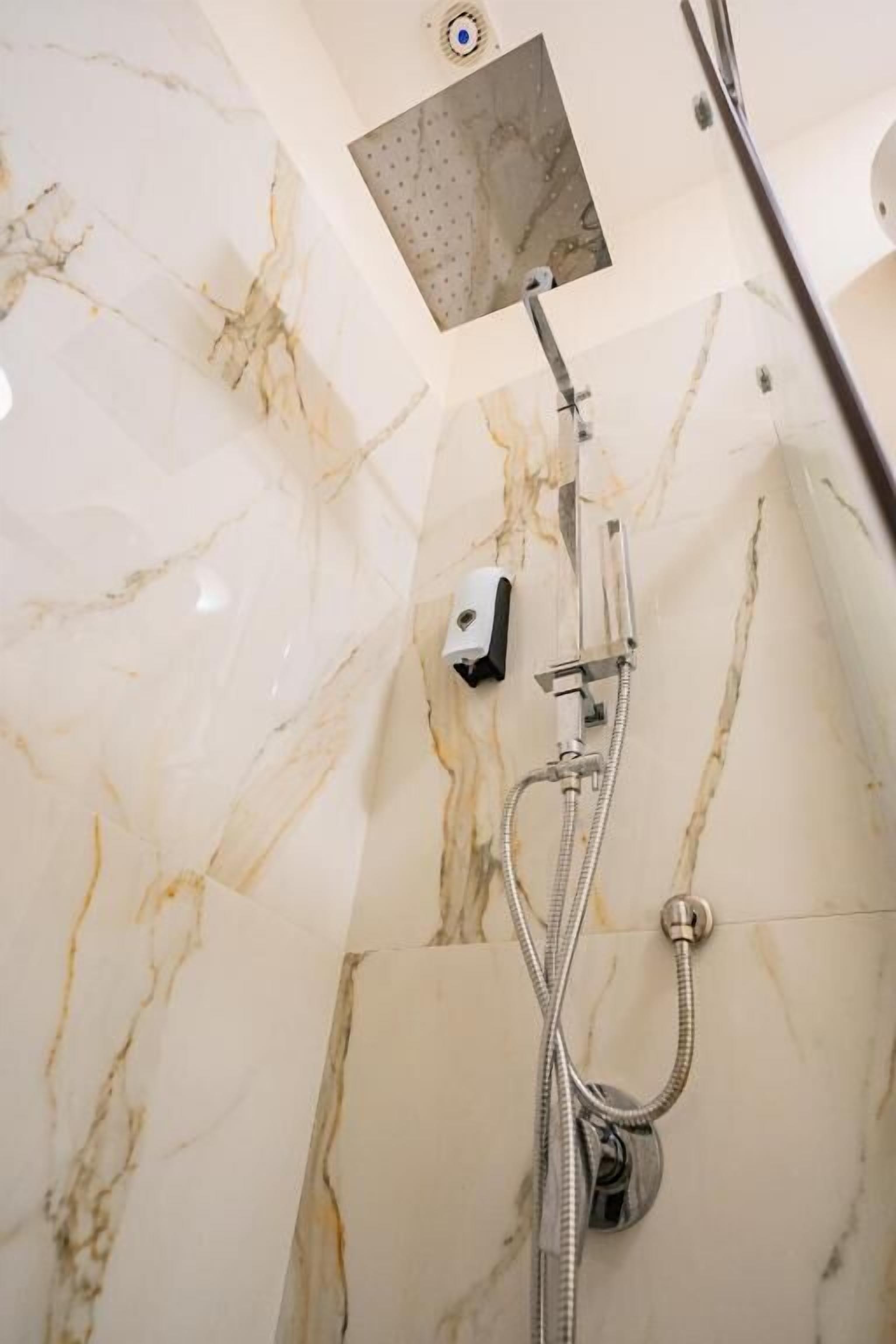 Een badkamer met een douche, marmeren wanden en een plafondlamp.
