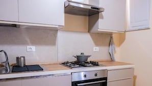 Cocina compacta con gabinetes blancos, estufa a gas, horno y ventana con persianas.