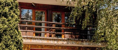 A multi-level wooden cabin with a stone facade, large windows, and a balcony with wicker furniture.