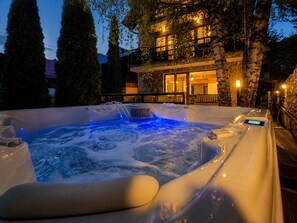 A hot tub with jets, surrounded by trees and a stone building with lights.