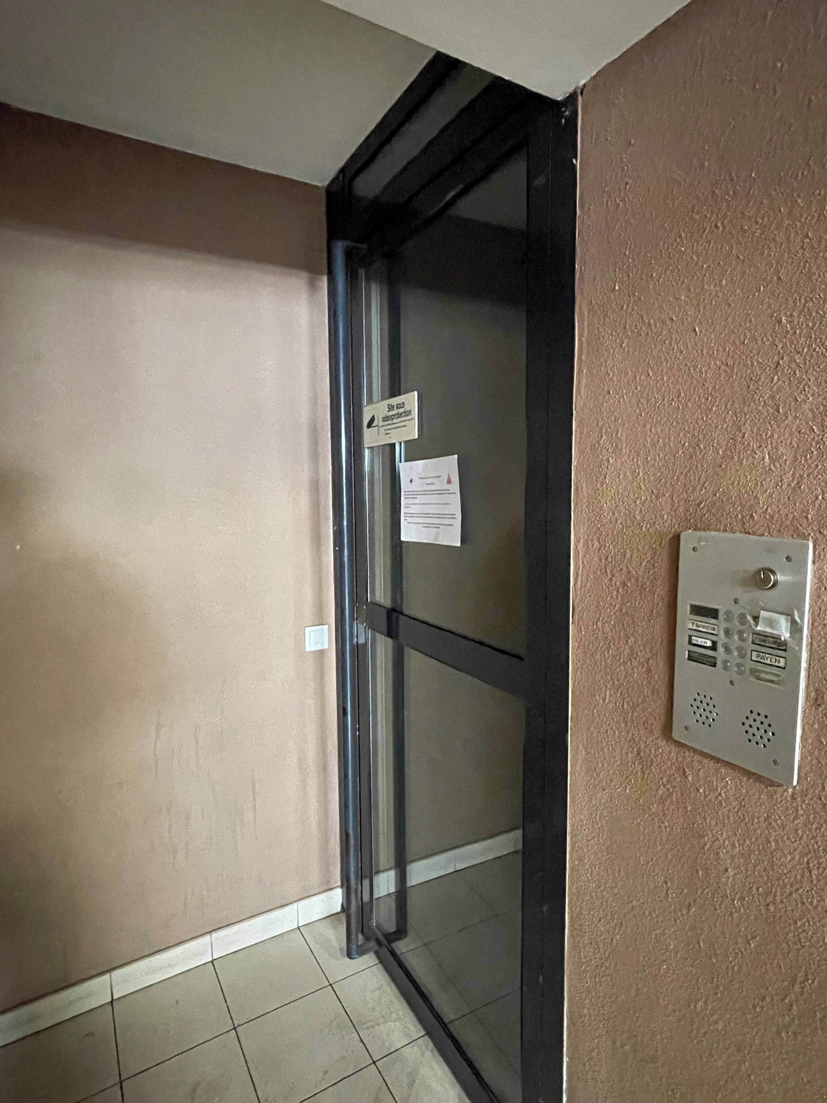 Une porte dotée d’un panneau en verre, un interphone fixé au mur et un panneau indiquant une zone de protection des eaux spécifique au site.