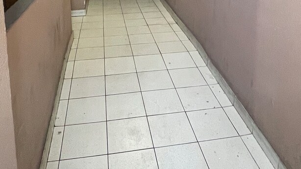 A corridor with tiled flooring and brown walls, leading to a door at the end.